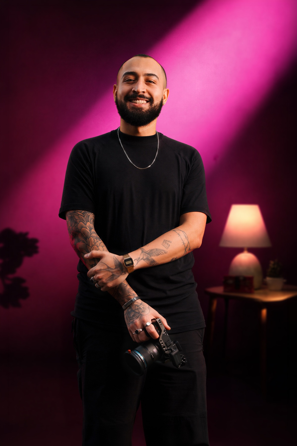 Lucas Has sorrindo, com a câmera na mão, sob luz rosa